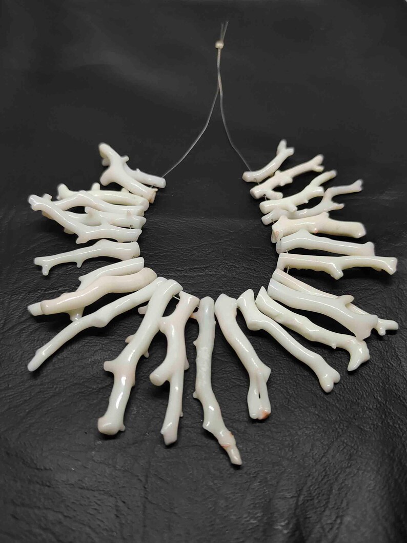 May include: A necklace composed of white coral branch beads. The coral pieces are strung together on a thin, clear cord, creating a natural and organic aesthetic. The beads have a textured surface and varying shapes.