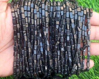 May include: A strand of black obsidian beads, each bead is a square shape with slightly rounded edges. The beads are strung together on a clear thread.