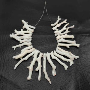 May include: A necklace of white coral branch beads, strung on a thin, clear cord. The coral pieces have a natural, organic shape, with a slightly textured surface. The background is a dark, solid color.
