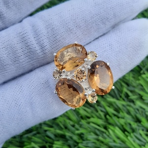 Puede incluir: Un anillo de plata con múltiples piedras preciosas de topacio de forma ovalada. El anillo presenta un grupo de piedras de topacio en tonos marrones y amarillos.