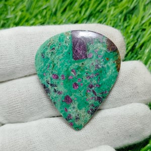 以下が含まれることがあります： ギターピックの形をした緑とピンクの宝石のカボション。宝石は、小さなピンクのインクルージョンが散りばめられた斑点模様をしています。