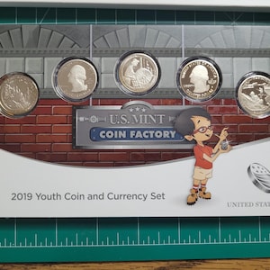 May include: A 2019 Youth Coin and Currency Set featuring five coins in protective cases. The packaging includes a cartoon illustration of a boy with glasses and the text "U.S. Mint Coin Factory". The background has a brick wall design.