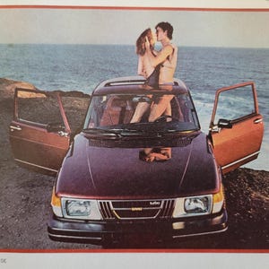 May include: A vintage burgundy Saab car with open doors, parked near the ocean. A couple is embracing through the sunroof. The image has a retro aesthetic, evoking a sense of freedom and romance. The car's headlights and grill are visible.