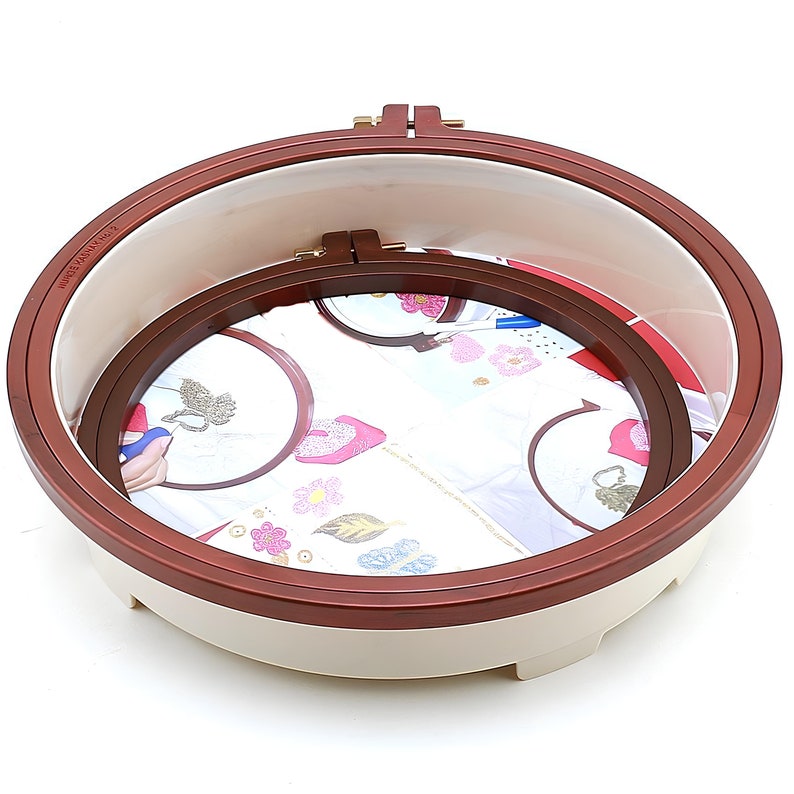 May include: A set of three round embroidery hoops with a brown wooden frame and a white plastic base. The hoops are nested inside each other, with the largest hoop on the bottom and the smallest hoop on top. The hoops are designed for embroidery projects.