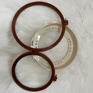 May include: Two brown wooden embroidery hoops with a white plastic hoop in the center. The hoops are nested together.