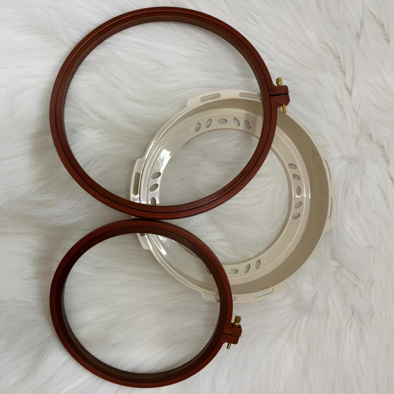 May include: Two brown wooden embroidery hoops with a white plastic hoop in the center. The hoops are nested together.