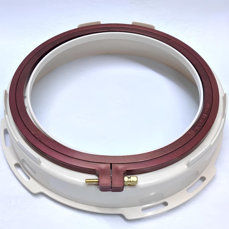May include: A white and burgundy embroidery hoop with a metal tightening mechanism. The hoop is designed for use with a sewing machine.