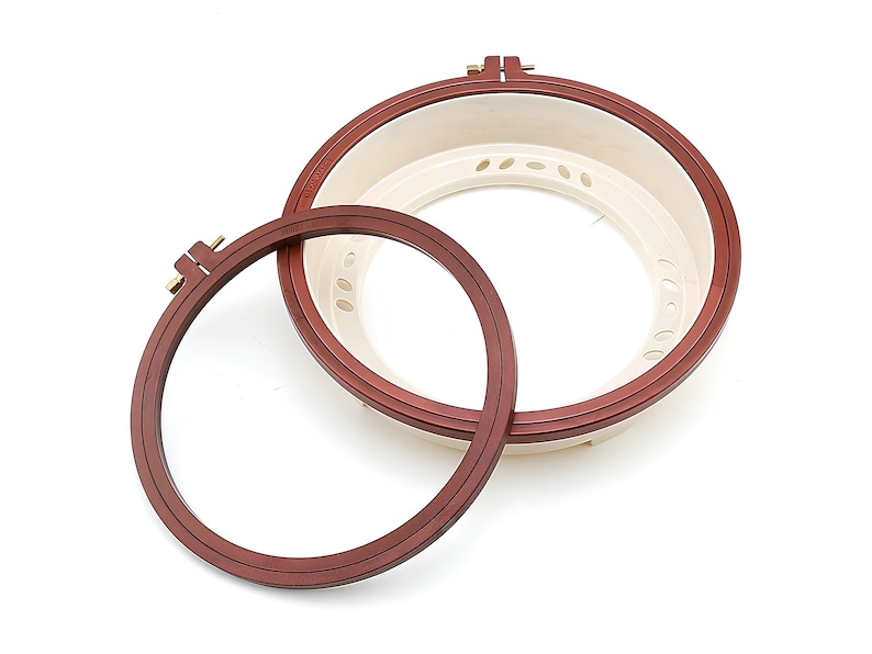 May include: Two embroidery hoops, one larger than the other, both with a brown wooden frame and a white plastic inner ring. The larger hoop has a screw-on mechanism.