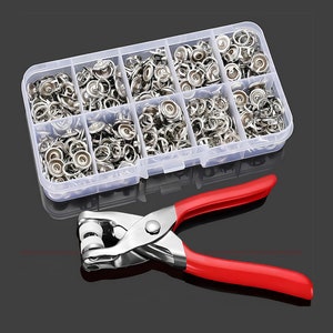 May include: A set of silver snap fasteners in a clear plastic container with a red-handled tool for attaching the fasteners.