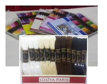 May include: A close-up of a set of embroidery floss in various colors, including white, cream, brown, and black. The floss is packaged in a clear plastic box with a red and white label that reads "L'Osiya Paris".