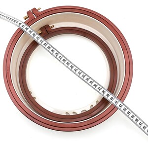 May include: A brown embroidery hoop with a white inner ring and a measuring tape across it. The tape measures 48 inches.