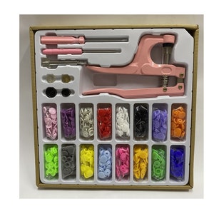 May include: A pink snap button press tool with two screwdrivers and 16 compartments of assorted colored plastic snap buttons.