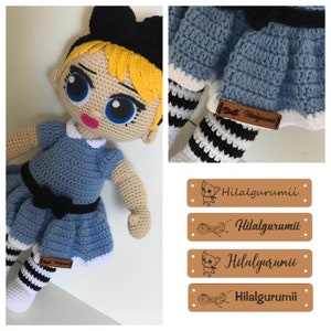 May include: A crocheted doll with blonde hair, blue eyes, and a blue dress with a black bow. The doll is wearing black and white striped stockings and a black headband with a bow. The doll is holding a brown leather tag with the text "Hilalgurumii".