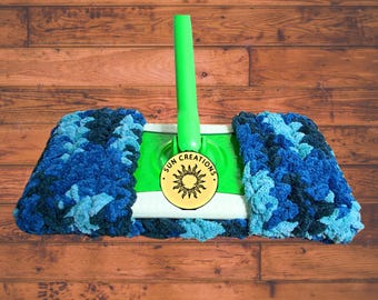 May include: A green mop with a blue and turquoise microfiber mop head. The mop head is attached to a green handle with a white and yellow circular label that says "SUN CREATIONS" with a sun graphic.