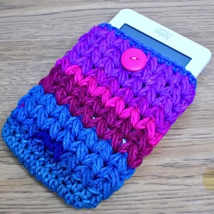 May include: A hand-crocheted e-reader case in blue, purple, and pink hues. The case has a button fastening and is designed to fit an e-reader device. The Kobo logo is visible on the e-reader screen.