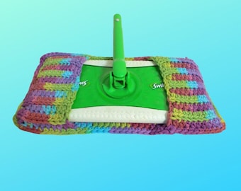 May include: A green and white Swiffer mop with a colorful, hand-crocheted cover. The cover features a mix of purple, yellow, green, and blue yarn. The mop handle is green, and the mop head is white.