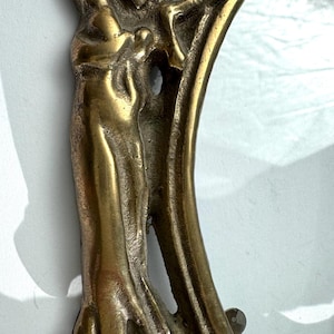 Peut inclure: Gros plan d'un cadre photo vintage en laiton. Le cadre présente un design orné avec une figure sculptée sur le côté. Le cadre a un insert en verre transparent et est probablement destiné à une petite photo ou œuvre d'art.