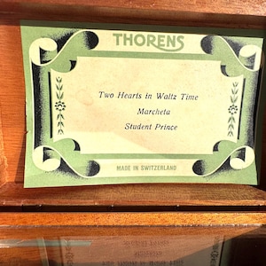 以下が含まれることがあります： 木製の箱で、内側に緑と黒のラベルが付いています。ラベルには上部に「THORENS」、テキスト「Two Hearts in Waltz Time」、「Marcheta」、「Student Prince」と書かれています。ラベルには「MADE IN SWITZERLAND」とも書かれています。