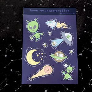 May include: A sheet of stickers with a space theme. The stickers feature green aliens, a rocket ship, a UFO, a planet, a crescent moon, and a comet with a donut. The text "beam me up some coffee" is at the top.