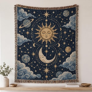 May include: A woven tapestry featuring a dark blue background with a central golden sun and crescent moon face. The design includes various planets, constellations, and swirling clouds in shades of gold and light blue, finished with a fringed edge.