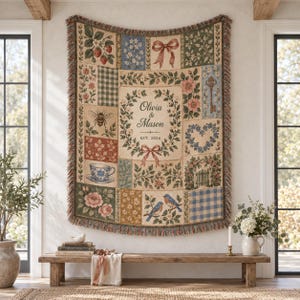 May include: A rectangular woven throw blanket featuring a patchwork design with botanical, floral, and vintage motifs. The center displays a floral wreath surrounding the text Olivia & Mason EST. 2026. The edges are finished with a fringed border.