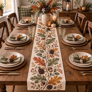 May include: A rectangular table runner featuring a printed pattern of autumn oak leaves, acorns, pinecones, and berries in shades of orange, green, and brown. The runner has a quilted texture and is centered on a wooden dining table with place settings.