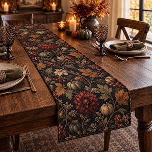 May include: A rectangular table runner featuring a dark black background with a repeating pattern of autumn-themed elements including orange and brown maple leaves, red berries, deep red dahlia flowers, and muted green and cream-colored pumpkins.