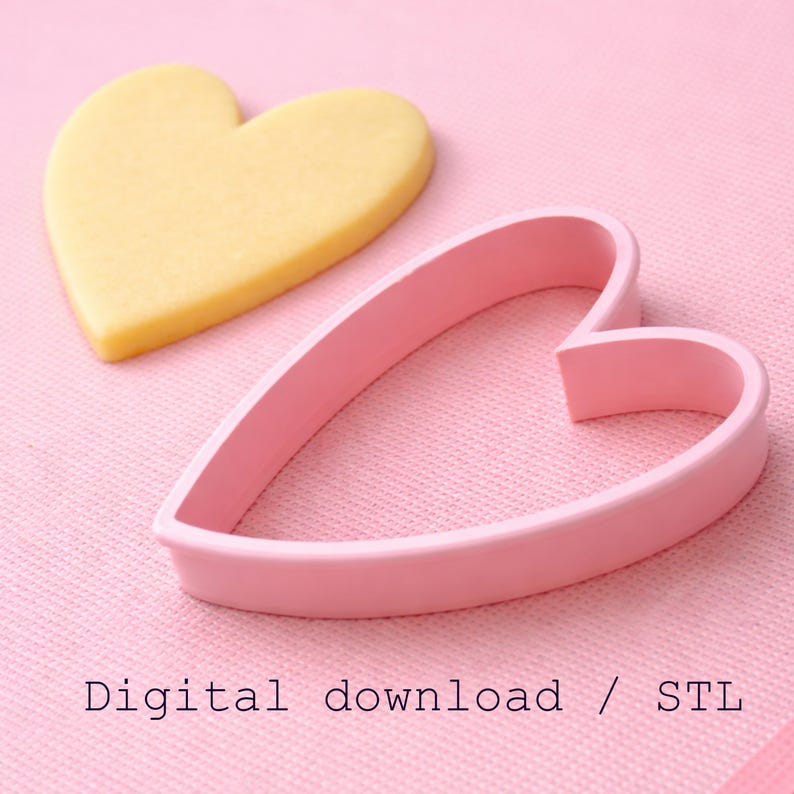 Puede incluir: Un cortador de galletas rosa en forma de coraz&oacute;n junto a una galleta en forma de coraz&oacute;n sobre una superficie rosa. La galleta es amarilla. El texto "Digital download / STL" est&aacute; en la parte inferior de la imagen.