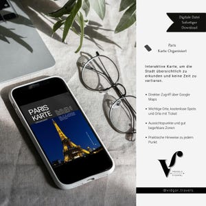 May include: A smartphone showing a digital map of Paris with the Eiffel Tower at night. The phone is beside round eyeglasses and a laptop on a light surface. The screen text reads "Paris Karte Organisiert."