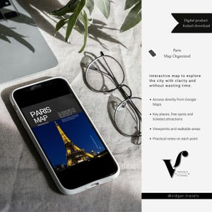 Puede incluir: Un smartphone muestra un mapa digital de París con la Torre Eiffel de noche. El teléfono está junto a unas gafas redondas y un portátil sobre una superficie clara. El texto de la imagen dice "Paris Map Organized" y "Descarga instantánea de producto digital."