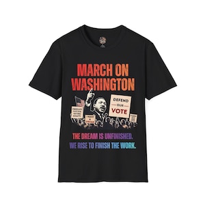 May include: A black short-sleeve t-shirt featuring a graphic of the March on Washington with Martin Luther King Jr. pointing upward. The text reads MARCH ON WASHINGTON, DEFEND OUR VOTE, FREEDOM JUSTICE VOTING RIGHTS, I HAVE A DREAM, THE DREAM IS UNFINISHED. WE RISE TO FINISH THE WORK.