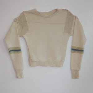 May include: A cream-colored sweater with blue and yellow stripes on the sleeves. The sweater has a crew neck and a ribbed hem.