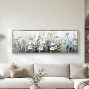 May include: A rectangular wall art piece featuring an abstract floral painting with white, blue, and gold tones. The artwork is enclosed in a thin gold frame and depicts a field of wildflowers with visible brushstrokes and textured paint layers.