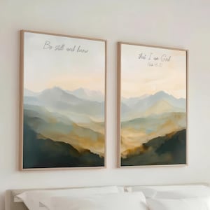 May include: Two vertical framed wall art prints featuring a watercolor-style mountain landscape in shades of blue, green, and gold. The left print displays the text Be still and know, while the right print displays that I am God Psalm 46:10.