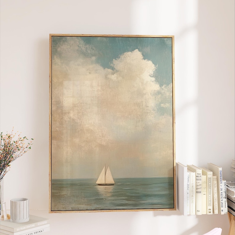 a large framed painting of a sailboat on the ocean, hanging on a wall next to a bookshelf filled with books.