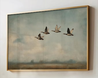 May include: A framed artwork featuring a flock of four ducks in flight against a muted blue sky. The painting has a vintage aesthetic with a gold-colored frame. The ducks are depicted with brown and white feathers.