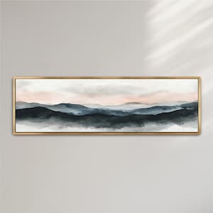 May include: A rectangular landscape painting with a gold frame. The artwork depicts a watercolor scene of layered mountains in shades of blue, gray, and black, with a soft pink and white sky. The painting is mounted on a white wall.