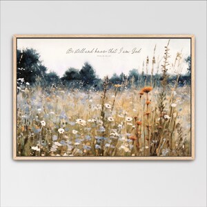 The image is a framed painting depicting a field of wildflowers, with a text overlay that reads "On stillness know that I am God" from the Bible verse Psalm 46:10.