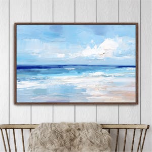 a framed painting of a serene ocean scene with a blue sky and white clouds, hanging on a white wall above a wooden chair.
