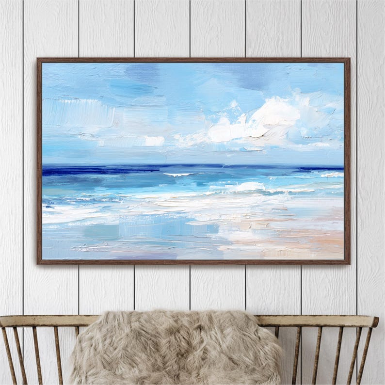 a framed painting of a serene ocean scene with a blue sky and white clouds, hanging on a white wall above a wooden chair.