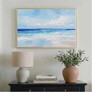 a painting of a serene ocean scene hanging on a wall above a black dresser with a lamp and a vase of greenery.