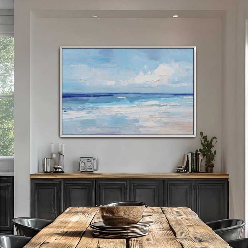 a large painting of a serene ocean landscape hanging on a wall above a wooden dining table. The table is set with plates and bowls, creating a cozy dining atmosphere.