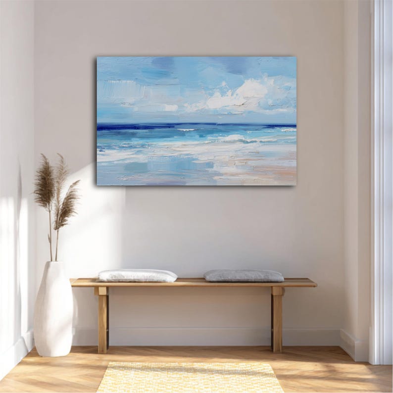 a serene beach scene with a wooden bench and a white vase with dried reeds, all set against a white wall with a painting of the ocean above it.