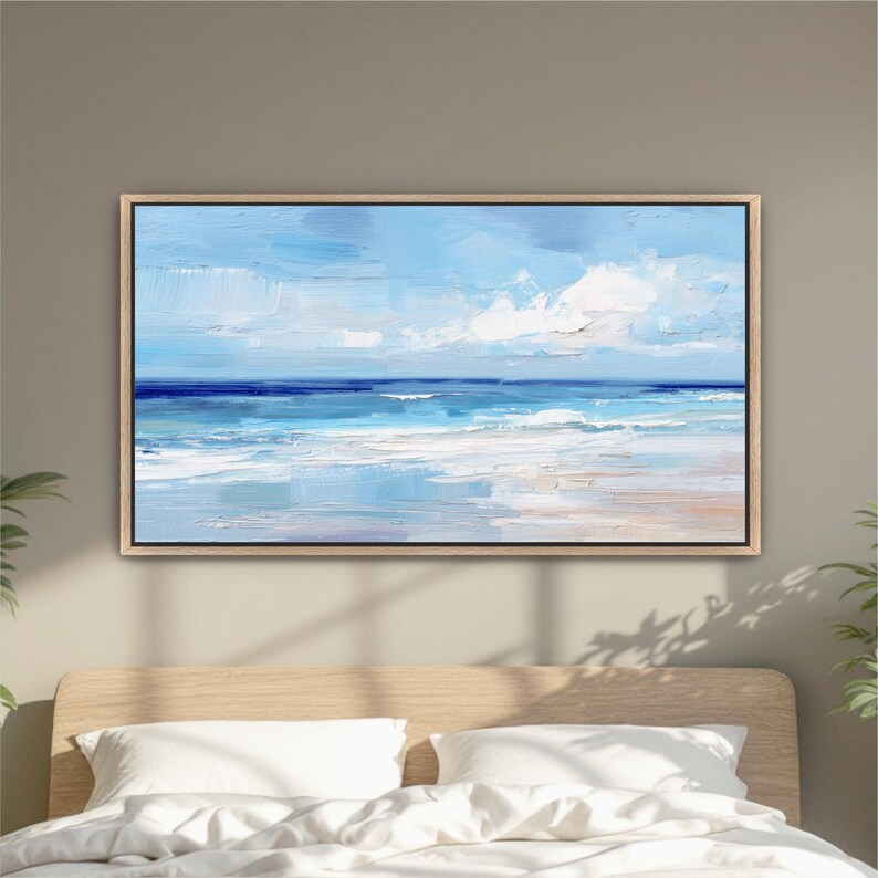 a large, framed painting of a serene ocean landscape hanging on a wall above a bed with white pillows.