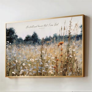 The image is a framed painting depicting a field of wildflowers, with a text overlay that reads "Be still and know that I am God" from Psalm 46:10.