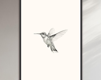 May include: A framed wall art print featuring a detailed black and white pencil sketch of a hummingbird in flight. The bird is centered on a plain off-white background, captured with fine lines and shading, enclosed within a thin black rectangular frame.