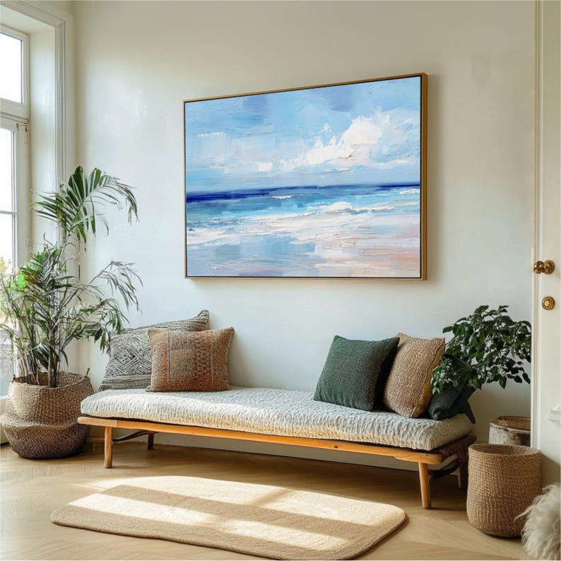 a living room with a large painting of a beach scene hanging on the wall above a couch with pillows. The room is decorated with potted plants and a rug, creating a cozy and inviting atmosphere.