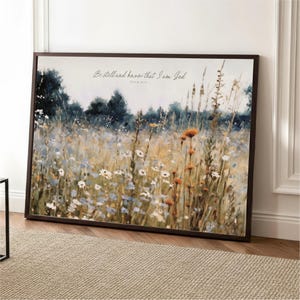The image is a framed painting depicting a field of wildflowers, with a text overlay that reads "Be still and know that I am God" from Psalm 46:10.