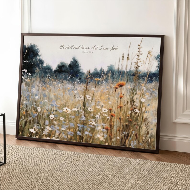 The image is a framed painting depicting a field of wildflowers, with a text overlay that reads "Be still and know that I am God" from Psalm 46:10.