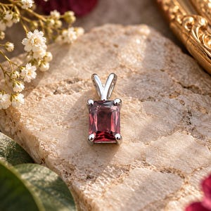 May include: A rectangular, deep red gemstone pendant set in a polished silver-toned metal prong setting. The pendant features a faceted cut that reflects light, with a simple silver bail at the top for attachment to a chain or necklace.